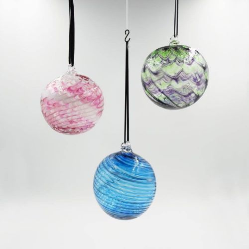 Three colorful glass ornaments hang from black ribbons against a light background, featuring swirls of pink, green, and blue.