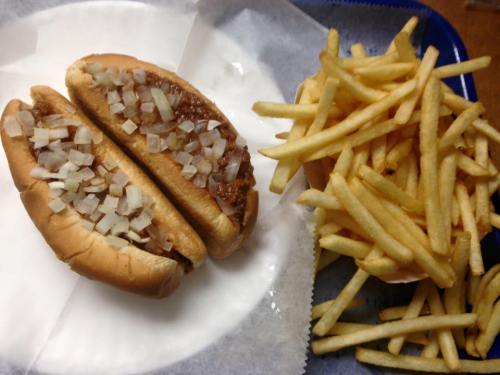 Two chili dogs topped with chopped onions on a plate, accompanied by a side of golden French fries.