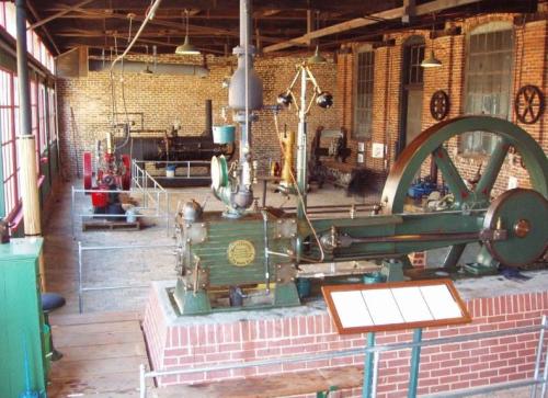 Historic industrial workshop featuring vintage machinery and brick walls, showcasing steam engines and equipment.