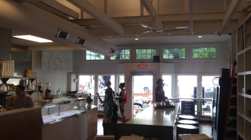 A cozy café interior with a counter, patrons ordering, and large windows letting in natural light.