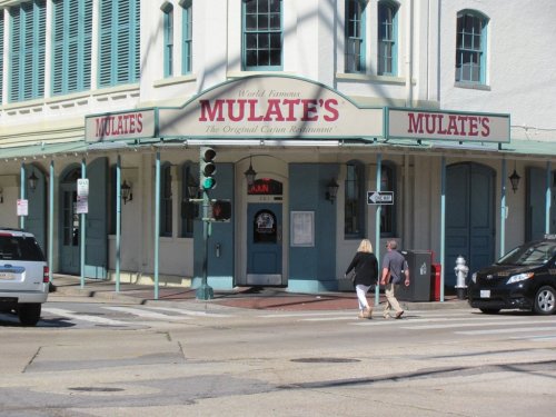 A couple walks across the street in front of Mulate's, a famous Cajun restaurant with a colorful sign.