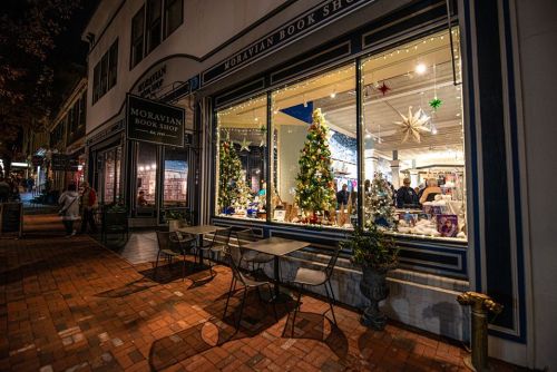 A cozy bookshop window decorated for the holidays, featuring Christmas trees and festive lights.