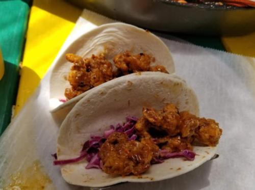 Two tacos filled with crispy shrimp and purple cabbage on a colorful background.