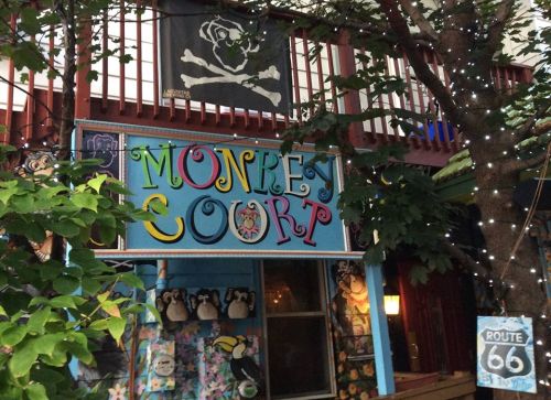 Colorful sign reading "Monkey Court" with pirate flag above, surrounded by trees and Route 66 sign nearby.