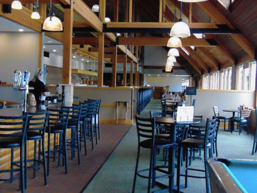 Interior of a spacious bar and restaurant with wooden beams, tables, and a pool table in the corner.