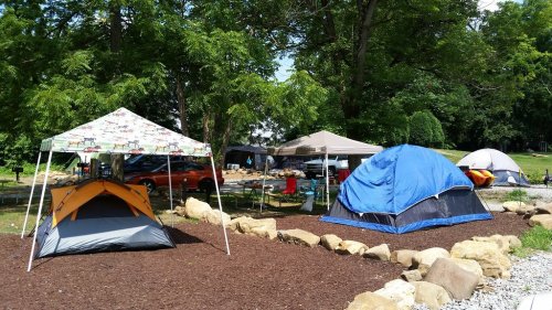 A campsite with various tents, canopies, and a gravel area surrounded by trees and rocks.