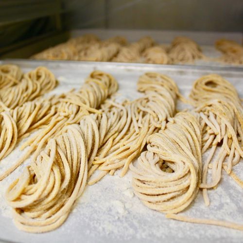 Freshly made pasta strands dusted with flour, arranged neatly on a tray.