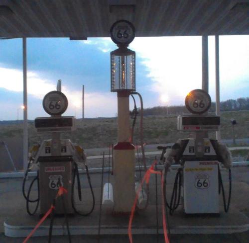 Two vintage gas pumps with "66" signage at a roadside station, set against a cloudy sky.