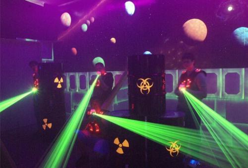 Three players in a laser tag arena with glowing green lasers and a space-themed backdrop featuring planets.