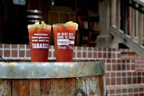 Two Bloody Mary cocktails with lime garnishes sit on a wooden barrel, with a rustic background.