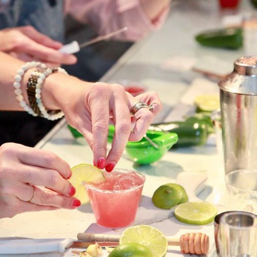 A close-up of hands preparing a cocktail with lime slices, a shaker, and fresh ingredients on a bar counter.