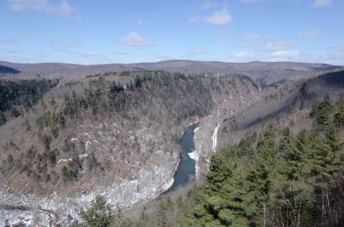 A scenic view of a winding river surrounded by wooded hills under a clear blue sky.