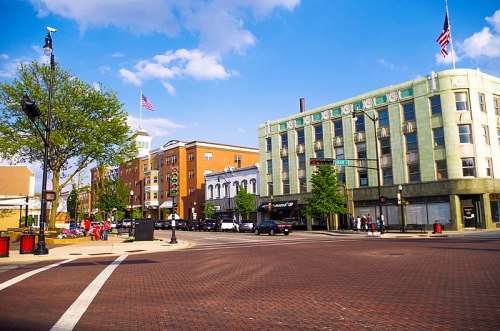 A vibrant downtown scene with shops, trees, and American flags under a blue sky.