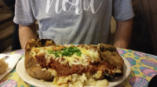 A large baked potato topped with chili, melted cheese, and green onions, served on a colorful table.