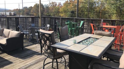 Outdoor seating area with tables and chairs, featuring a fire pit, surrounded by trees in autumn colors.