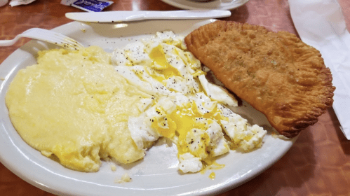A plate with scrambled eggs, creamy grits, and a golden-brown fried pastry.