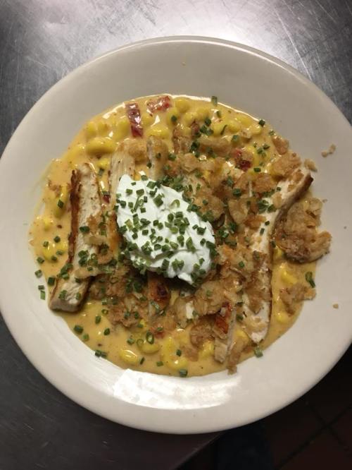 A creamy pasta dish topped with grilled chicken, crispy onions, and a dollop of sour cream, garnished with chives.