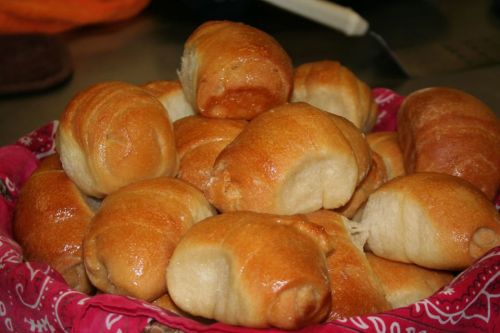 A basket filled with golden-brown, freshly baked rolls, arranged neatly with a decorative cloth underneath.
