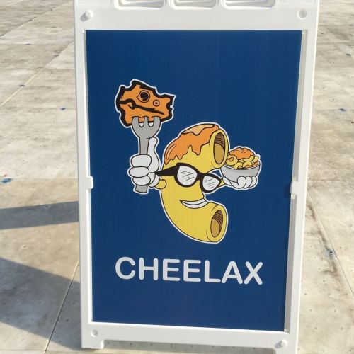 A sign featuring a cartoon macaroni character holding cheese and a fork, with the word "CHEELAX" below.