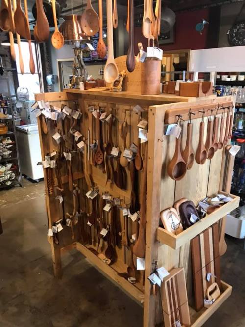 A wooden display stand filled with various handcrafted wooden kitchen utensils and tools, hanging and arranged neatly.