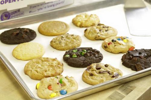 A tray of assorted cookies, including chocolate chip, peanut butter, and colorful candy cookies, on a white background.