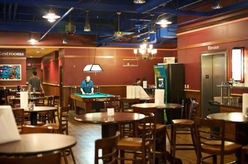 A casual dining area with pool tables, arcade games, and wooden tables in a warmly lit space.