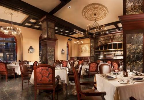 Elegant restaurant interior with ornate decor, chandeliers, and well-set tables. Warm lighting creates a cozy atmosphere.