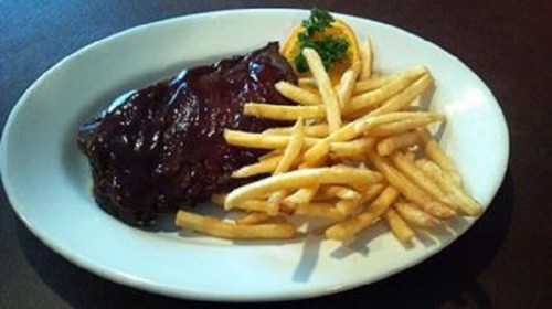 A plate featuring a grilled steak topped with barbecue sauce, accompanied by a side of golden French fries and a garnish.