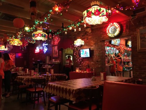 Cozy restaurant interior with colorful lights, stained glass lamps, and checkered tables, creating a festive atmosphere.