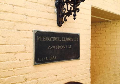 Plaque on a yellow brick wall reading "International Exports, Ltd. 779 Front St. Estab. 1868."