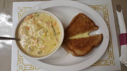 A bowl of creamy vegetable soup next to a grilled cheese sandwich on a white plate.