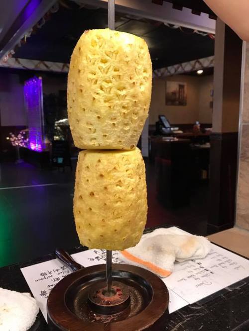 Two halves of a pineapple are skewered vertically on a stand, ready for serving in a restaurant setting.