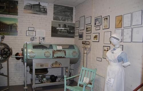 A vintage medical exhibit featuring an old machine, a mannequin in a nurse's outfit, and historical photos on the wall.