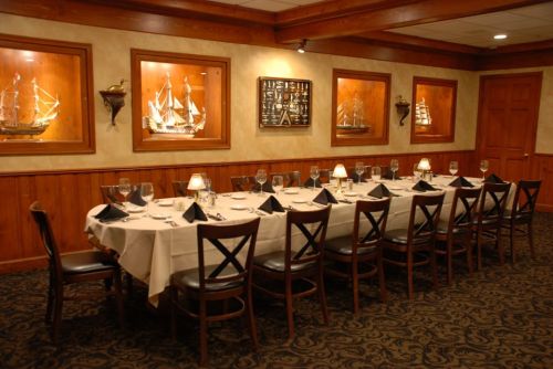 A long dining table set for a formal meal, surrounded by wooden walls and displays of model ships.
