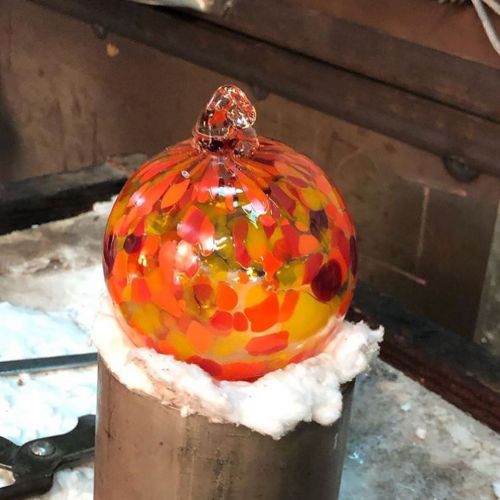 A colorful glass orb with orange, red, and yellow patterns sits on a workbench, surrounded by tools and cotton.