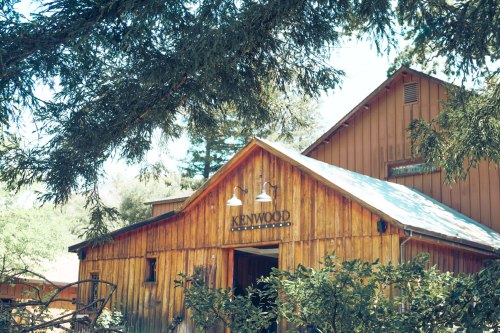 A rustic wooden building with a sign reading "Kenwood" surrounded by trees and greenery.