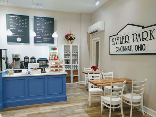 Cozy café interior with a blue counter, coffee machines, and seating area, featuring a sign for Sayler Park, Cincinnati.