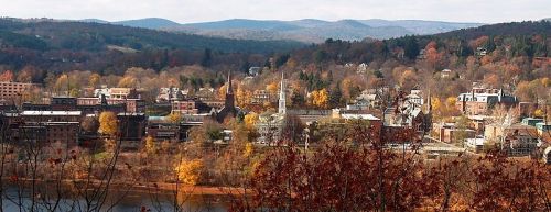 A scenic view of a small town surrounded by autumn foliage and mountains in the background.