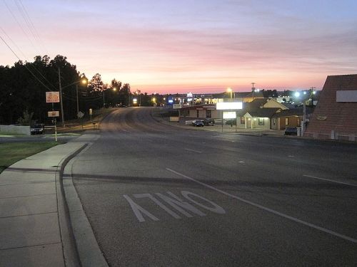 A quiet street at dusk, with a colorful sky and distant buildings illuminated by streetlights.