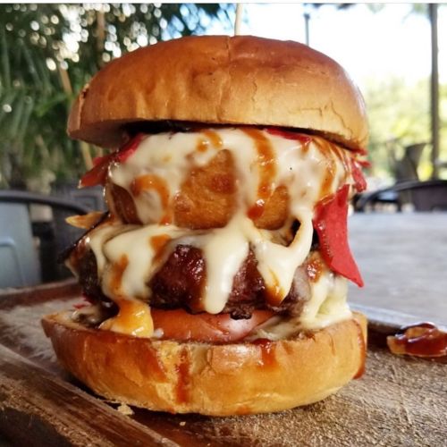 A towering burger with a juicy patty, melted cheese, crispy onion rings, and sauce, served on a toasted bun.