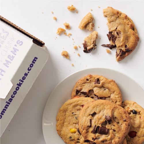 A plate of chocolate chip cookies with a few broken pieces, next to a box labeled "Insomnia Cookies."