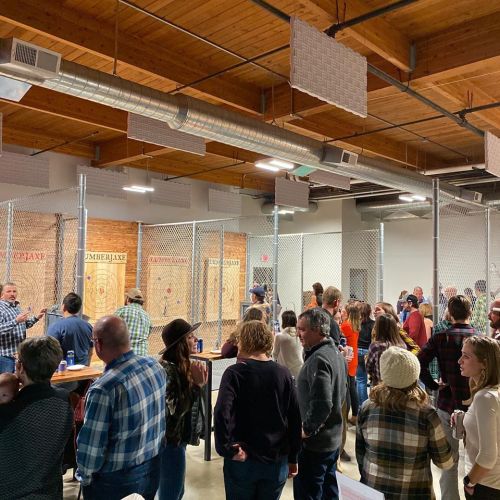 A lively indoor axe-throwing venue with a crowd enjoying the activity and wooden targets in the background.