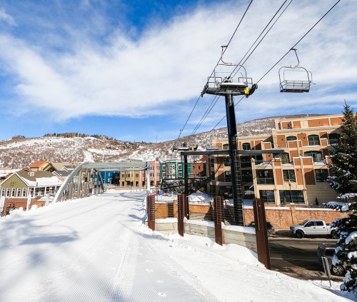 A snowy landscape featuring a ski lift, buildings, and a clear blue sky in a mountain resort area.