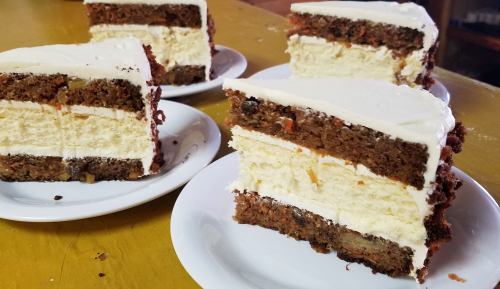 Slices of layered carrot cake with cream cheese frosting on white plates, set on a yellow table.