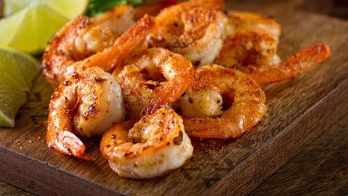 Grilled shrimp seasoned with spices, served on a wooden platter with lime wedges.