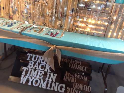 A display of jewelry on a turquoise table with a wooden sign that reads "Turn Back Time in Wyoming."
