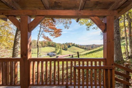 View from a wooden porch overlooking rolling hills and colorful autumn trees under a clear blue sky.
