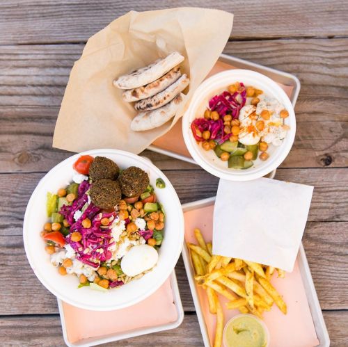 A colorful meal featuring a salad bowl with falafel, pickled veggies, and fries on a wooden table.