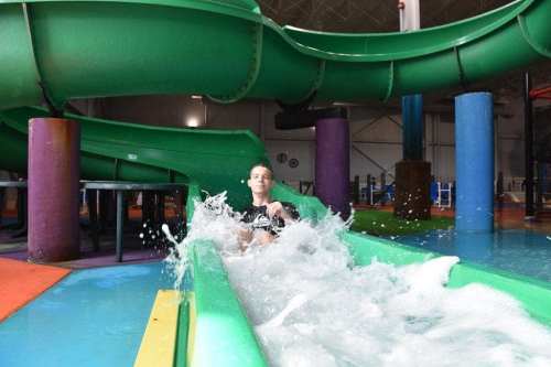 A person splashes into the water at the end of a colorful water slide in an indoor water park.