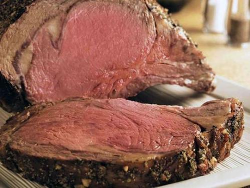 A close-up of a perfectly cooked prime rib, showcasing its juicy, pink interior and seasoned crust.